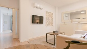 Un salon moderne avec un canapé, un téléviseur, une petite table et un miroir.