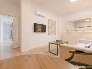 Ein modernes Wohnzimmer mit Sofa, Fernseher, kleinem Tisch und Spiegel.