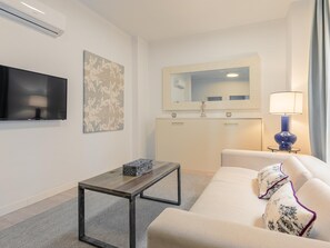 Una camera d'albergo moderna con una TV a schermo piatto, uno specchio decorativo, un comodino, un divano e una lampada.