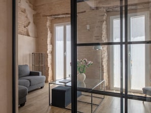 Ein modernes Wohnzimmer mit einer Couch, einem Glastisch und Blick durch eine Glastür.