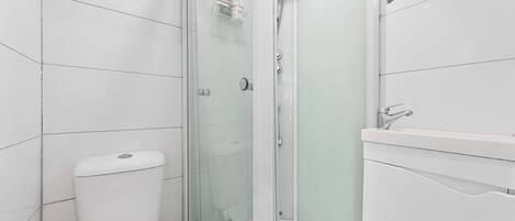 Een badkamer met een douchecabine, toilet en een wastafel met spiegel.