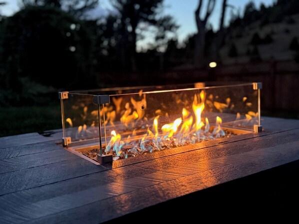 A rectangular glass fire feature with a metal frame, set on a wooden deck.