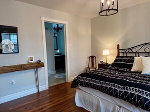 A bedroom with a bed, a nightstand, a lamp, a chair, a mirror, and a wooden shelf.