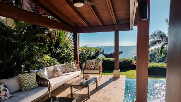A covered outdoor seating area with a pool, a sofa with patterned cushions, and a view of the sea. - Villa With Private Pool and sea View in Samaná (Samaná)