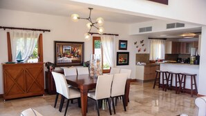 A dining area with a wooden table and chairs, a chandelier, and a kitchen visible in the background. - Villa With Private Pool and sea View in Samaná (Samaná)