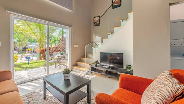 Ein modernes Wohnzimmer mit Fernseher, Sofa und einer Treppe, die in ein Obergeschoss führt.