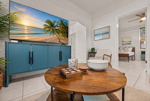 A dining area with a wooden table, a blue cabinet, and a painting of a beach scene. - 3-Min Walk to Sunset • Foosball • Pet Friendly (Indian Rocks Beach)
