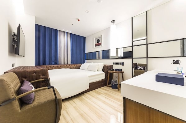 Una habitación de hotel con cama, sofá, escritorio, espejo y televisor en la pared.