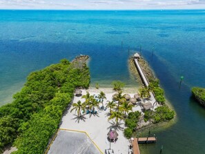 An aerial view of a tropical beach resort with a paved walkway, palm trees, and a pier extending into the water. - Coastal Retreat, Pool, Marina, Ocean View, FL Keys (Tavernier)