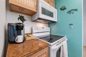 A kitchen with a microwave, coffee maker, and stove, wooden cabinets, and a teal wall with decorative items. - Coastal Retreat, Pool, Marina, Ocean View, FL Keys (Tavernier)