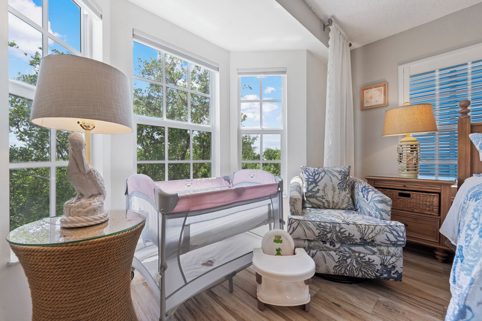 Une chambre équipée d’un berceau, d’une chaise haute, d’une chaise et d’une table de chevet avec une lampe.