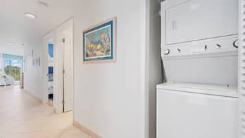 Un couloir d’hôtel avec une porte donnant sur une chambre, un tableau encadré accroché au mur et un appareil électroménager blanc, peut-être un lave-linge, dans un coin.