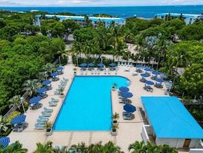 A resort with a central swimming pool surrounded by sun loungers and umbrellas, with palm trees and a view of the ocean. - Coastal Retreat, Pool, Marina, Ocean View, FL Keys (Tavernier)