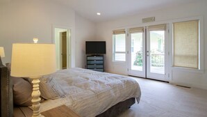 A bedroom with a bed, a TV, a lamp, and a sliding glass door leading to a balcony. - Spacious 4BR country retreat nestled in redwoods and apple orchard (Occidental)