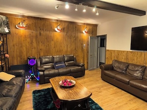 Ein modernes Wohnzimmer mit einer Wandpaneele aus Holz, Ledersofas, einem Couchtisch mit Obstschale und einem Lautsprecher mit farbigen Lichtern.