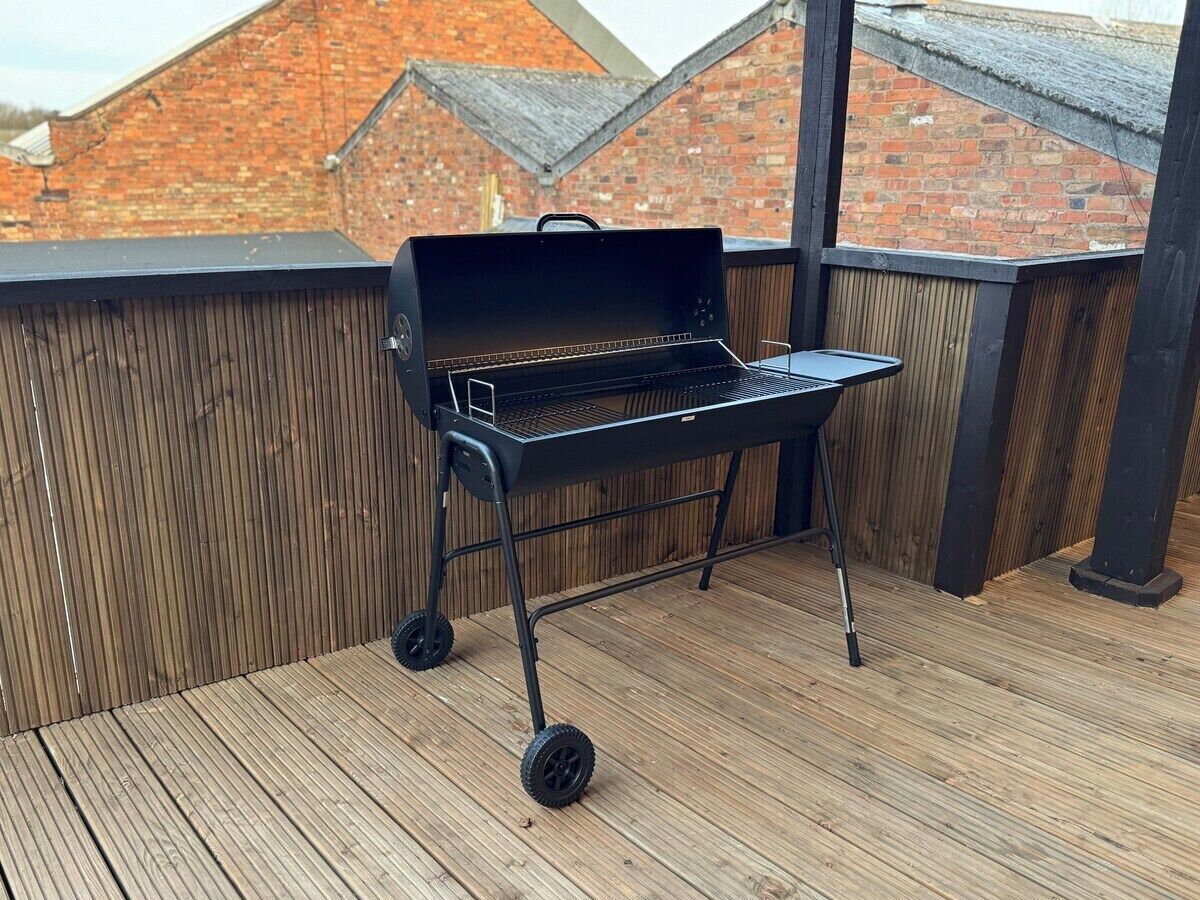 A portable barbecue grill on a wooden deck with a brick wall in the background.