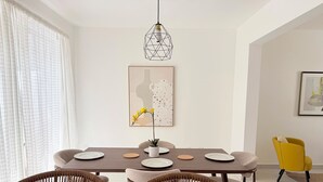 A dining area with a table, chairs, a hanging light fixture, and artwork on the wall. - Modern 2BR Oasis/Semi-Private Pool (Punta Cana)
