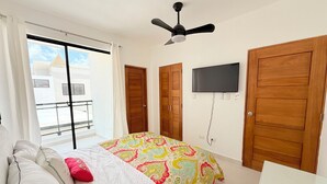 A bedroom with a bed, a ceiling fan, a TV mounted on the wall, and a balcony with a railing. - Modern 2BR Oasis/Semi-Private Pool (Punta Cana)