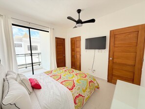 Ein Schlafzimmer mit einem Bett, einem Deckenventilator, einem an der Wand befestigten Fernseher und einem Balkon mit Geländer.