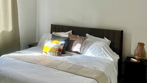 A neatly made bed with a headboard, a bedside table with a remote control, and a decorative vase. - Modern 2BR Oasis/Semi-Private Pool (Punta Cana)