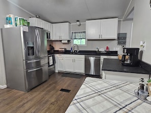 A modern kitchen with stainless steel appliances, white cabinets, and a plaid rug.