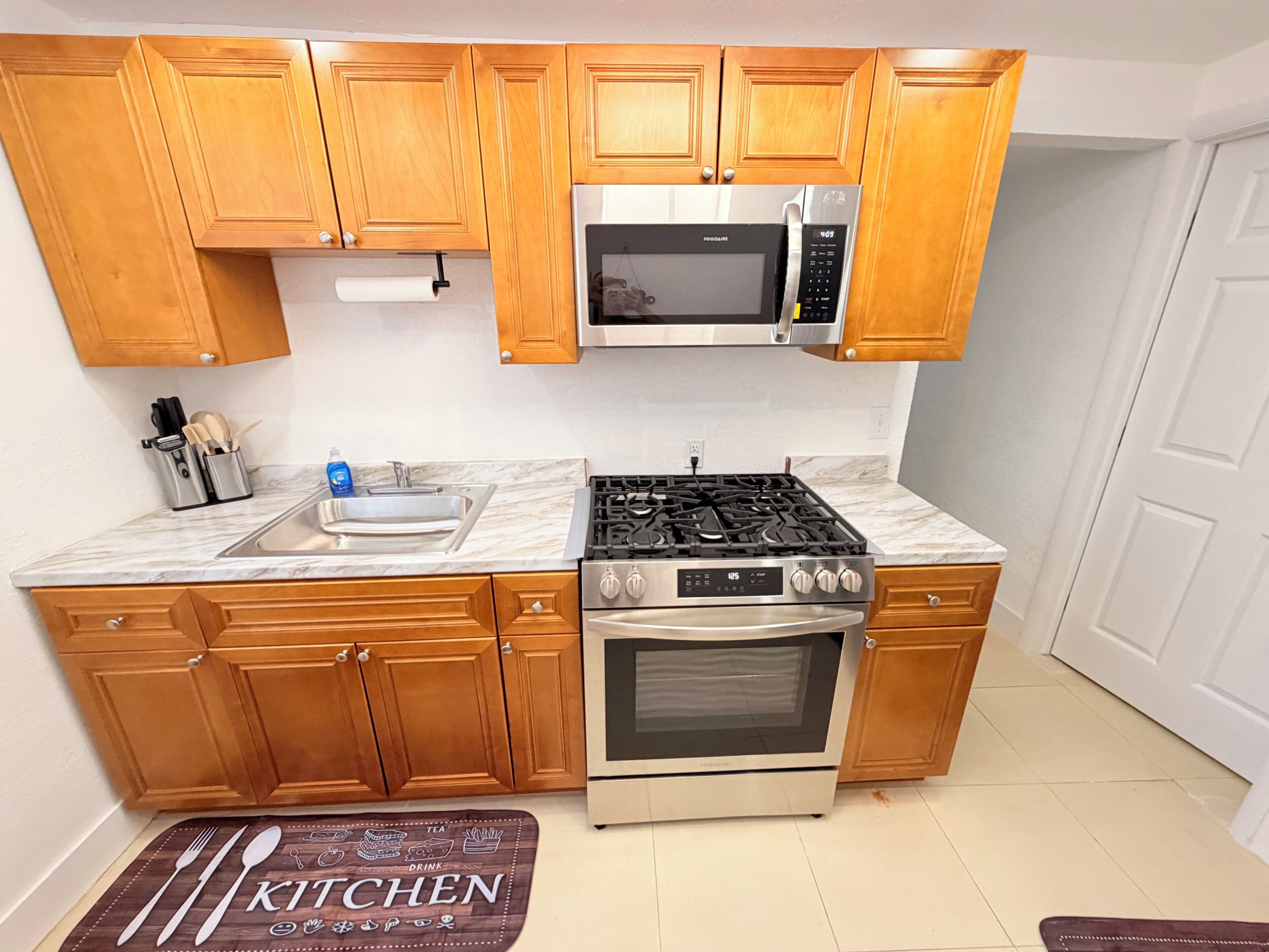 A kitchen with wooden cabinets, a stainless steel sink, a microwave, a gas stove, and an oven.