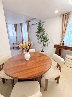 Una mesa de comedor redonda de madera con seis sillas, un florero con flores secas y una planta en maceta.