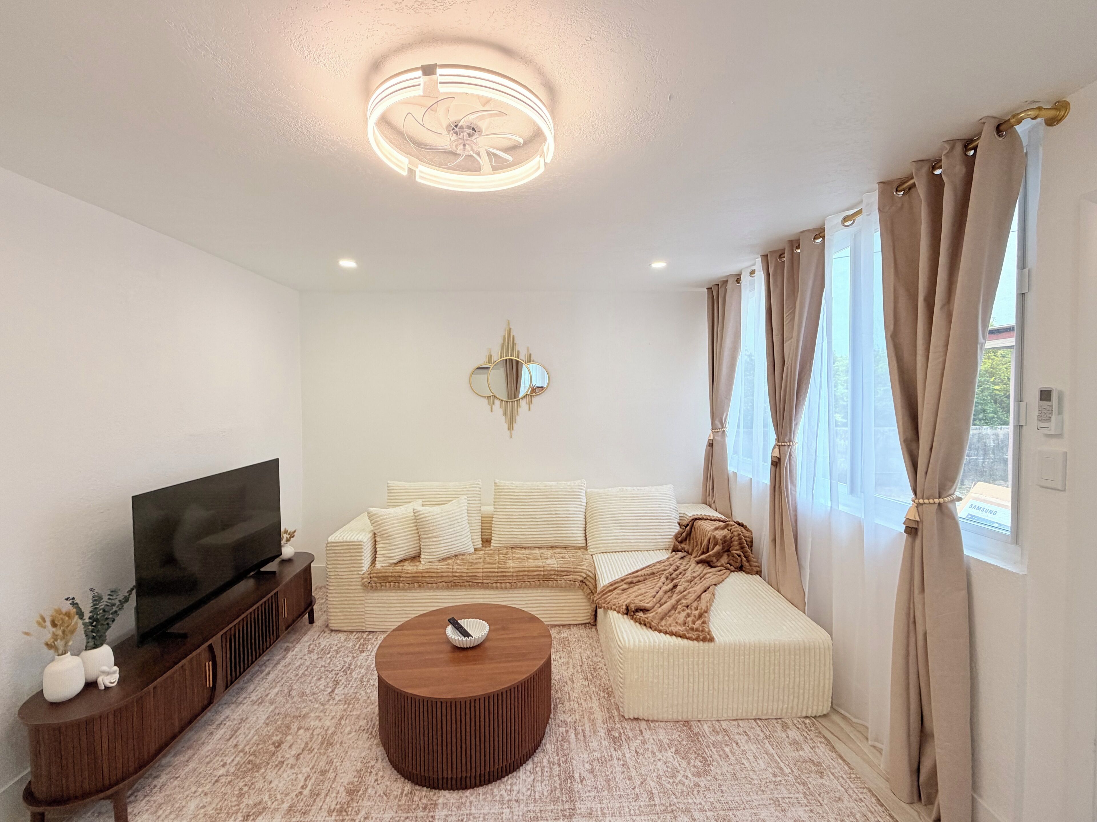 A modern living room with a flat-screen TV, a sofa, a coffee table, and a ceiling fan.