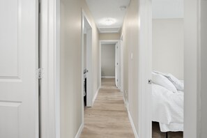 Ein schmaler Flur mit Holzboden führt zu einem Schlafzimmer mit einem Bett und einem Nachttisch.