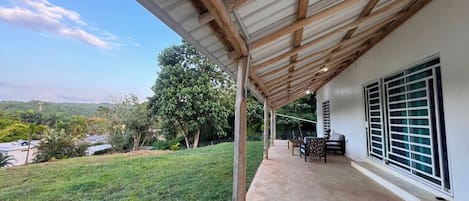 A covered outdoor area with a concrete floor, a wooden pergola, and a view of a grassy landscape with trees and hills.