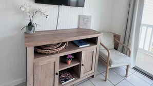 Una stanza con una TV a schermo piatto montata, un mobile basso in legno con ripiani, una pianta in vaso e una sedia.