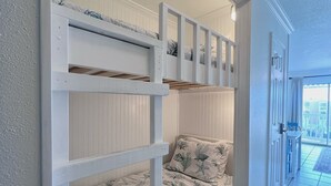 Un letto a castello con biancheria a tema nautico, una porta bianca e vista su un balcone.