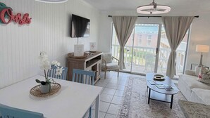 Un soggiorno moderno con zona pranzo, una televisione a schermo piatto montata a parete e un balcone con tende.