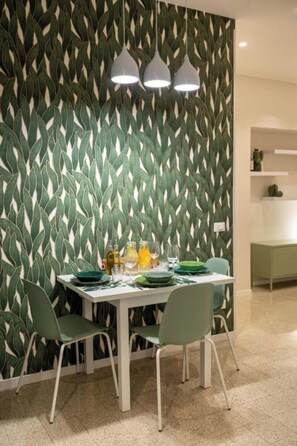 A dining area with a table set for four, chairs, and a wall with a leaf pattern. - Four-Bedroom Holiday Home (Roma)