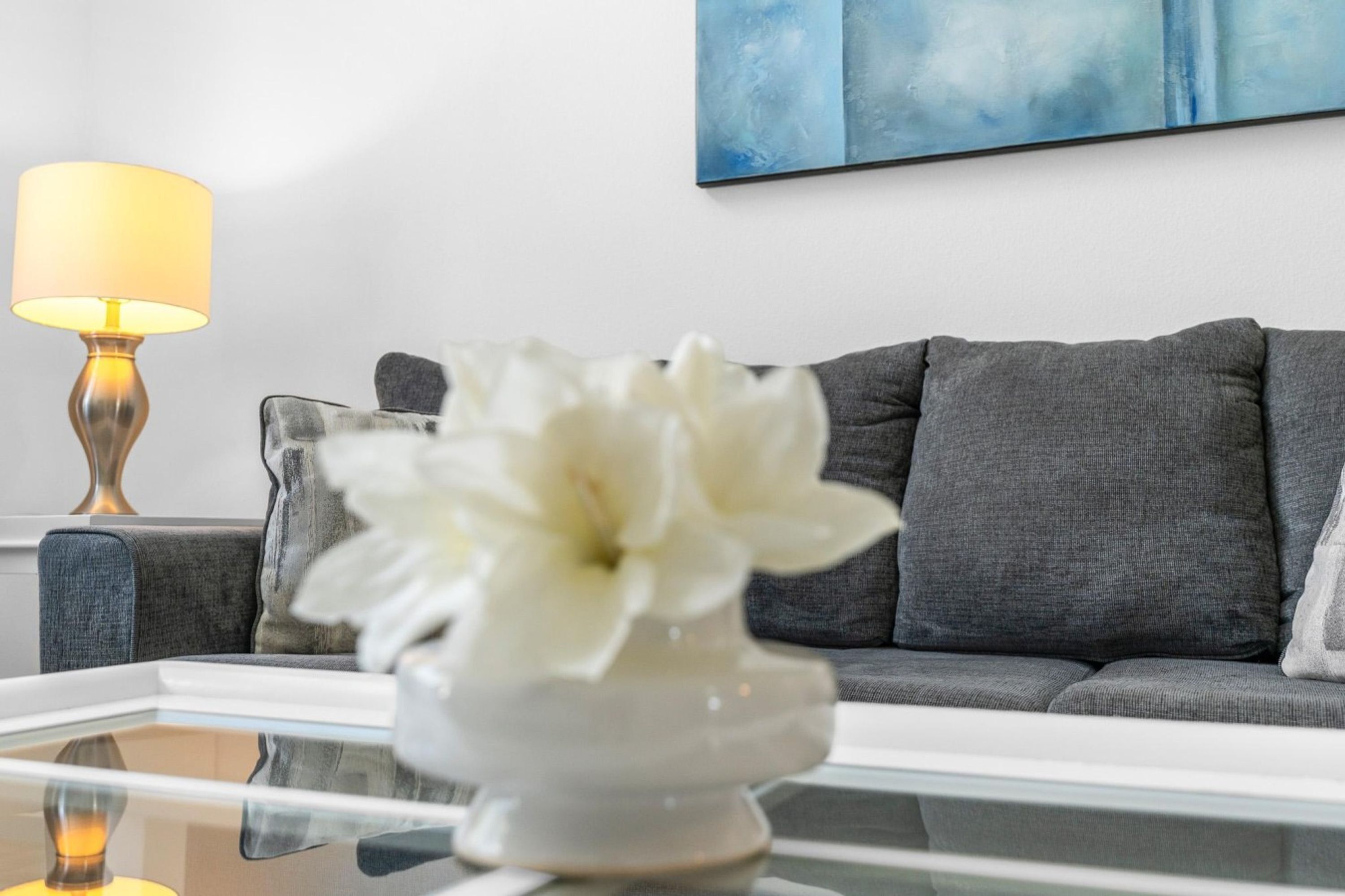 A living room with a sofa, a table with a vase of flowers, and a lamp.