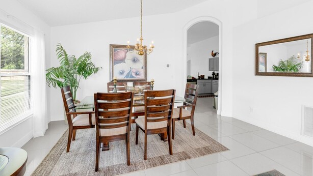 A dining area with a round table, six chairs, a chandelier, and a large painting on the wall. - Beautiful 4bdr With Private Pool Gated Community (Almont)