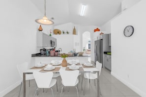 A modern kitchen with white cabinets, a dining area with white chairs, and a clock on the wall. - Beautiful 4bdr With Private Pool Gated Community (Almont)