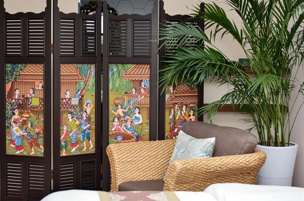A room with a woven sofa, a large potted plant, and traditional artwork on the wall.