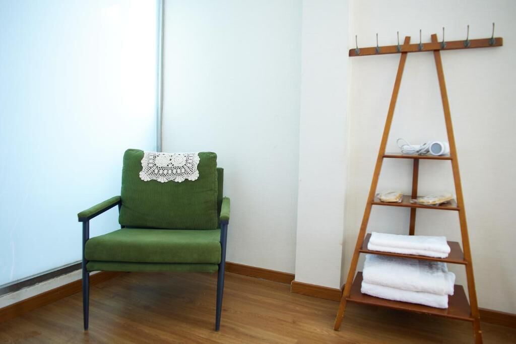 A green chair with a lace cover, a wooden shelf with towels, and a wooden floor.