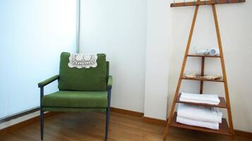 A green chair with a lace cover, a wooden shelf with towels, and a wooden floor.