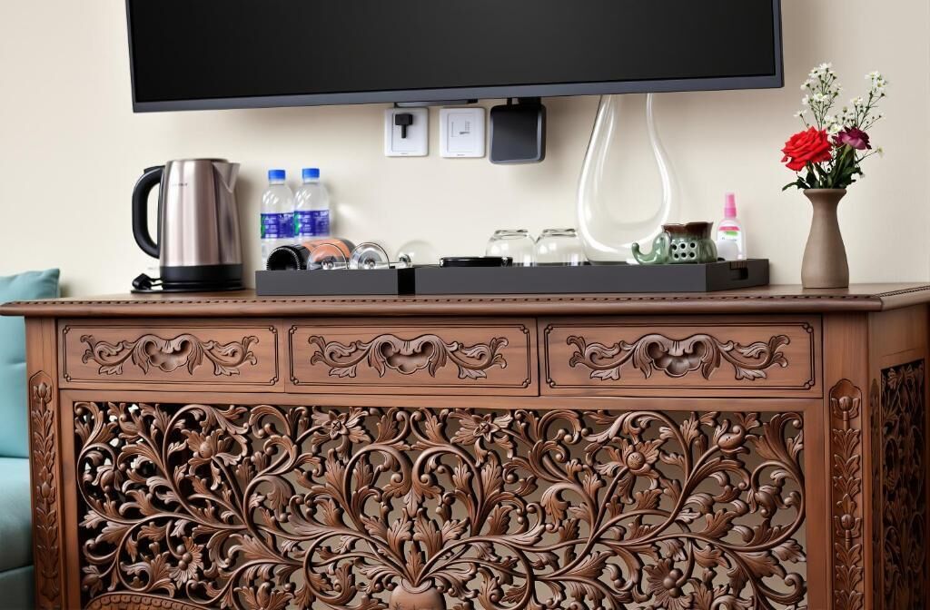 A wooden cabinet with intricate carvings, a flat-screen TV mounted above, and a vase with flowers on the right.