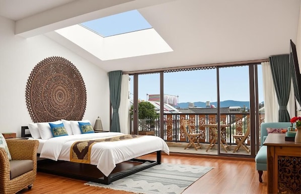 Quarto com claraboia, janelas amplas, cama, cadeira e varanda com vista.