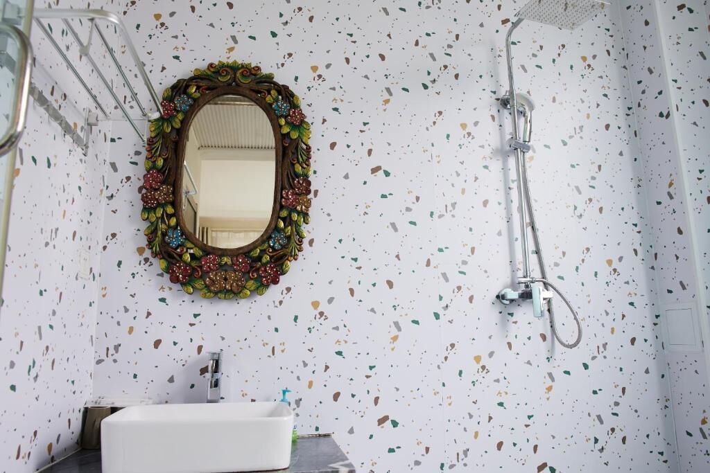 A bathroom with a white sink, a shower, and a mirror with a decorative frame.