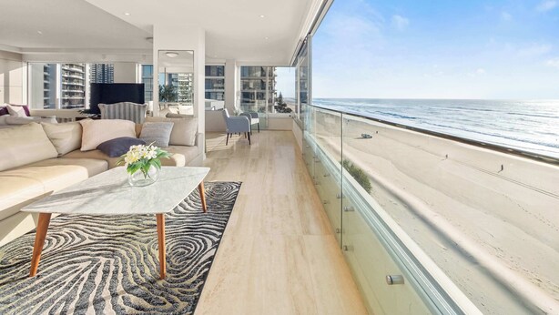 A modern living room with a sofa, coffee table, and a view of the beach. - Sea Below, Sun Above by Aryve (Main Beach)