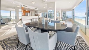 A modern interior with a round table, grey chairs, and a view of the ocean. - Sea Below, Sun Above by Aryve (Main Beach)