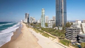 A coastal cityscape with high-rise buildings, a sandy beach, and a clear blue sky. - Sea Below, Sun Above by Aryve (Main Beach)