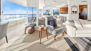A modern living room with a view of the ocean, a balcony, and a kitchen area. - Sea Below, Sun Above by Aryve (Main Beach)