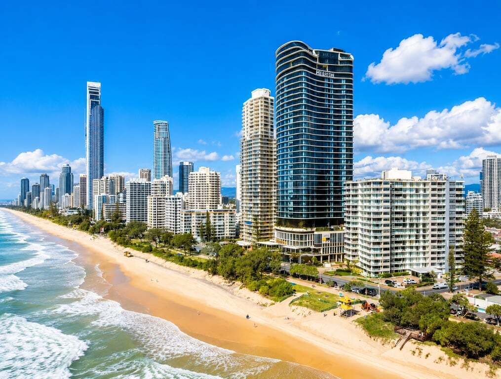Paesaggio costiero con grattacieli, una spiaggia sabbiosa e un cielo azzurro limpido.