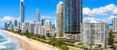 A coastal cityscape with high-rise buildings, a sandy beach, and a clear blue sky.