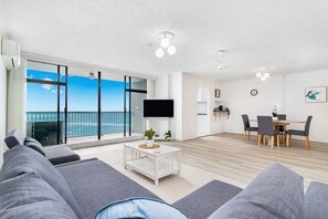 Ett modernt vardagsrum med en stor TV, en matplats och en balkong med utsikt över havet.